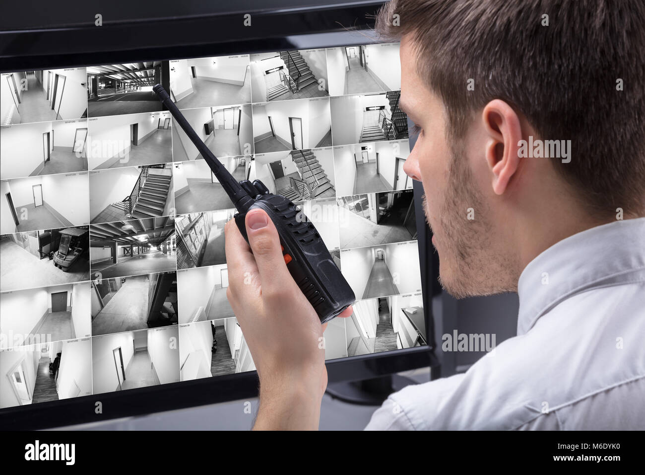 Young Male Security Guard Talking On Walkie-talkie While Monitoring Multiple CCTV Footage On Computer Stock Photo