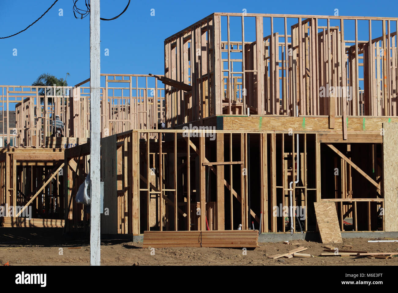 Several new two-story homes under construction, just framed, with skeletal walls built of 2 x 4 lumber; blue sky behind, power poles, on sunny day. Stock Photo