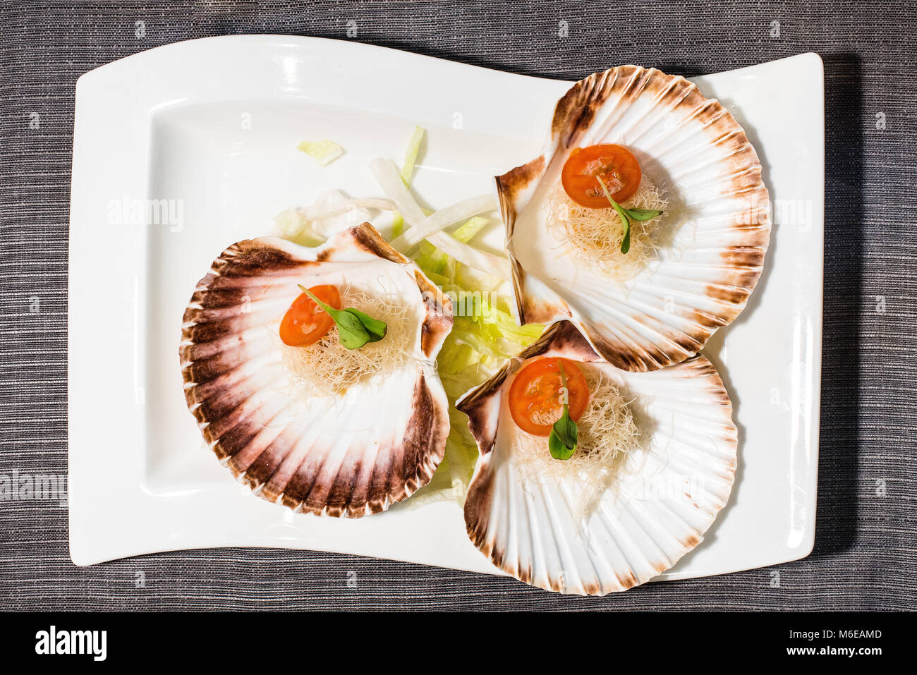 Coquilles Saint Jacques cooked on the plate served in shells with cherry tomatoes and soncino salad Stock Photo
