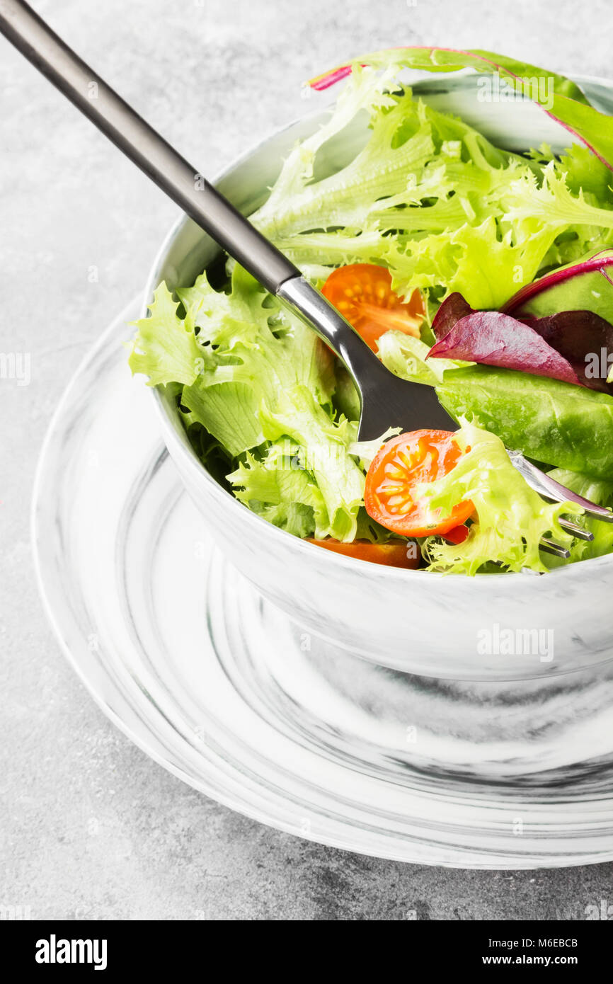 The dietary mixed greens salad (mesclun, mache, lettuce) and cherry tomatoes in a bowl on a light background Stock Photo