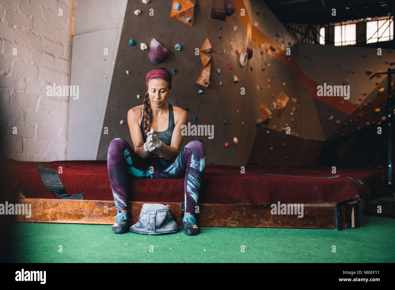 Woman at a wall climbing gym applying magnesium chalk powder on hands from a bag. Artificial bouldering wall in the background. Stock Photo