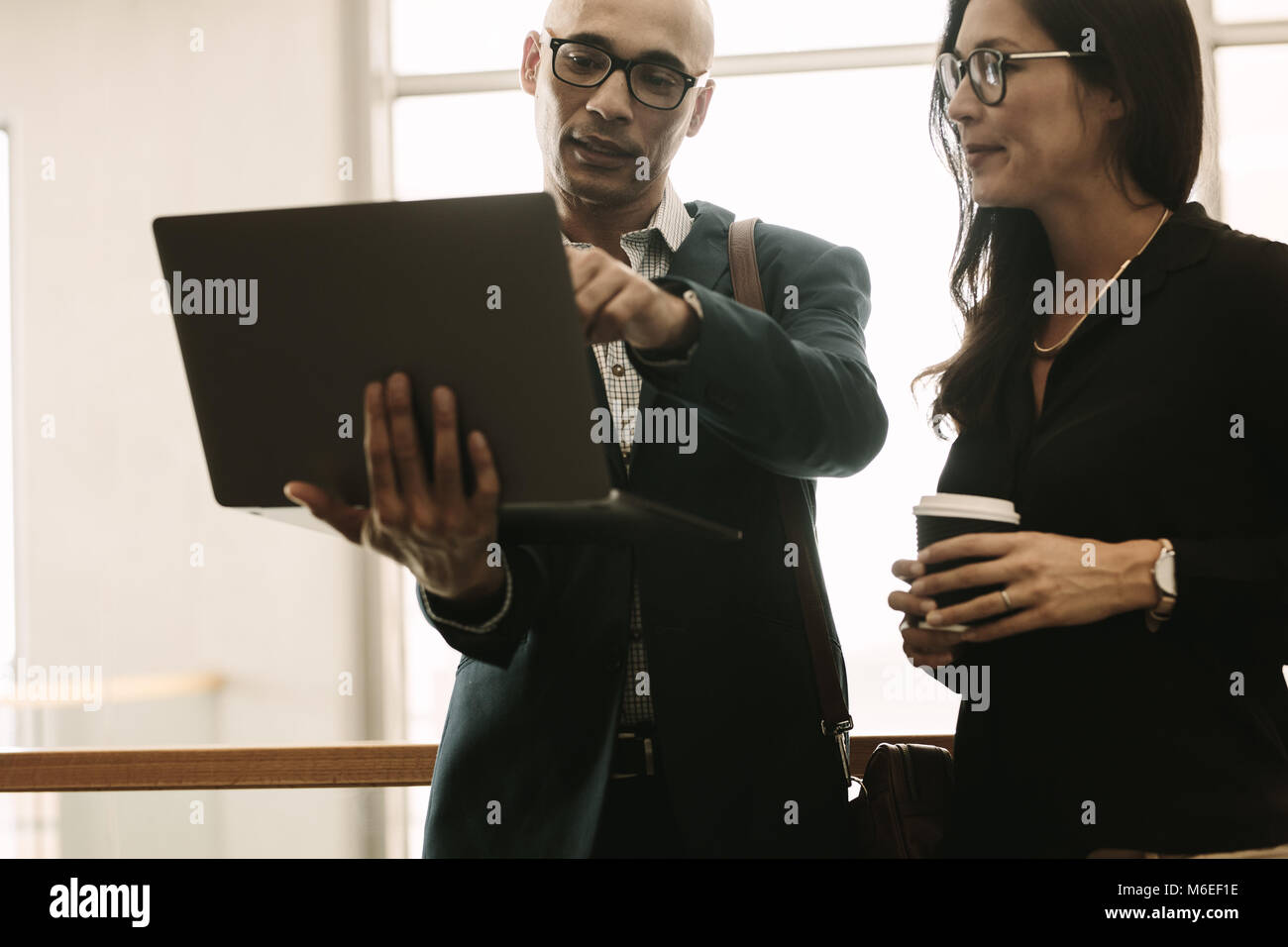 Businessman pointing at laptop and discussing something with coworker while standing at office. Business team working together in office, discussing s Stock Photo