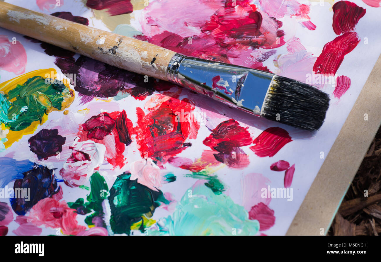 Raw Art artist's brush dipped in a variety of colored paints, resting