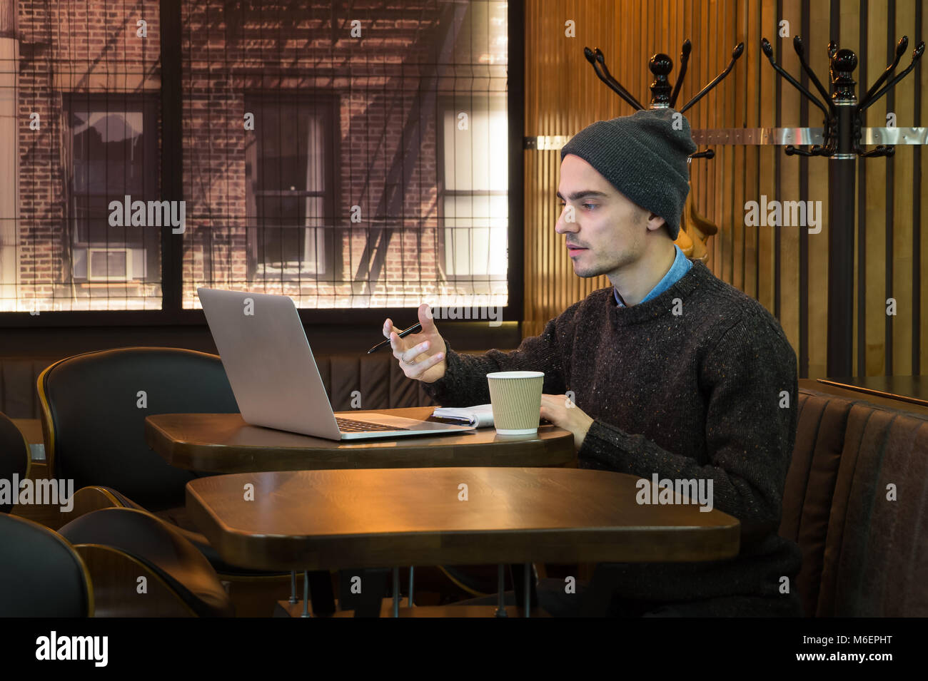 Man speaks online in cafe via internet messenger on computer. Young male person explains something, teaches or talks with help of web long distance ca Stock Photo