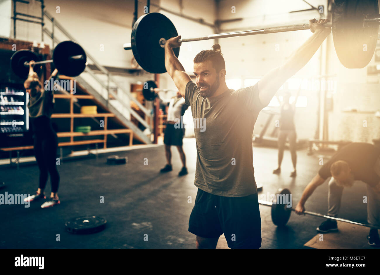 Fit young man lifting heavy weights above his head during a workout