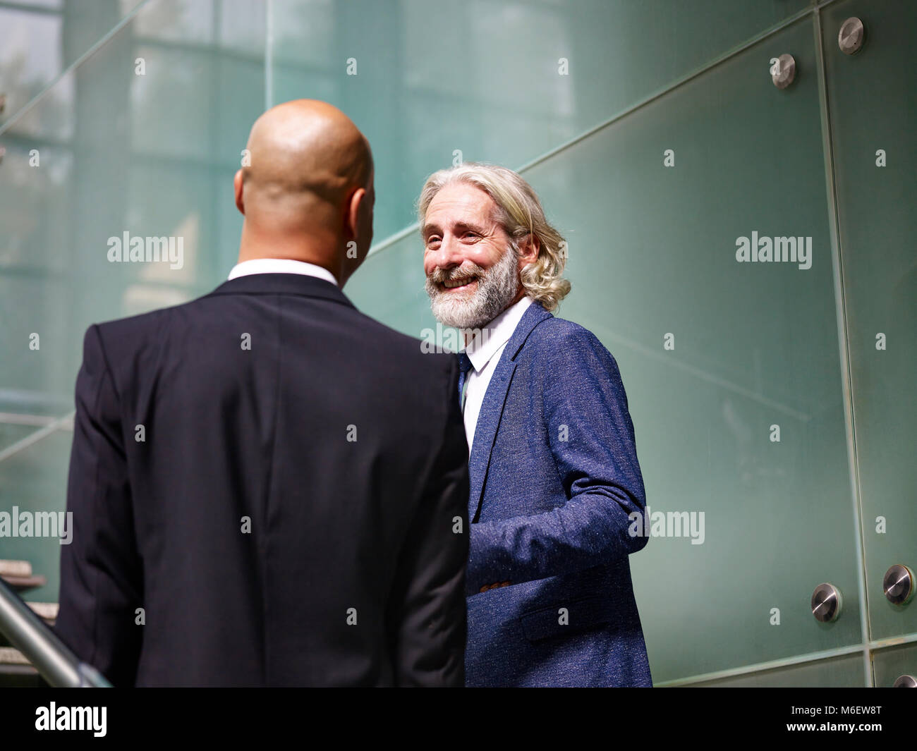 caucasian and latino corporate executives having a conversation while ascending stairs in modern office building. Stock Photo