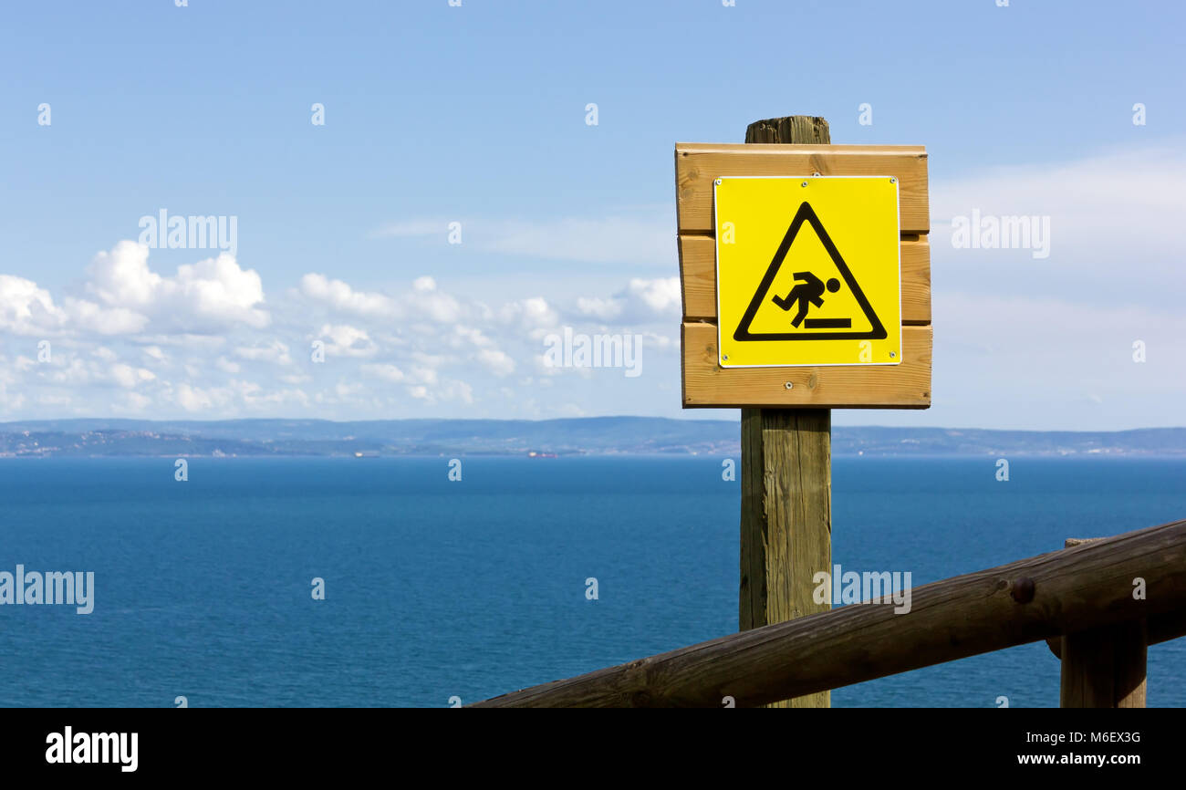 Yellow danger sign over the wooden fence of a seaside panoramic trail Stock Photo