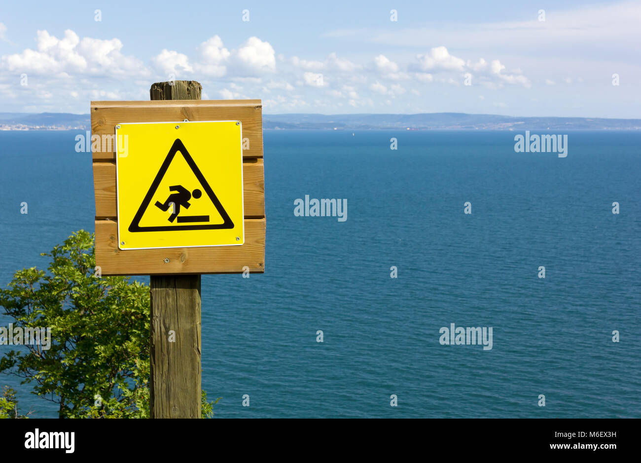 Yellow danger sign over the wooden fence of a seaside panoramic trail Stock Photo