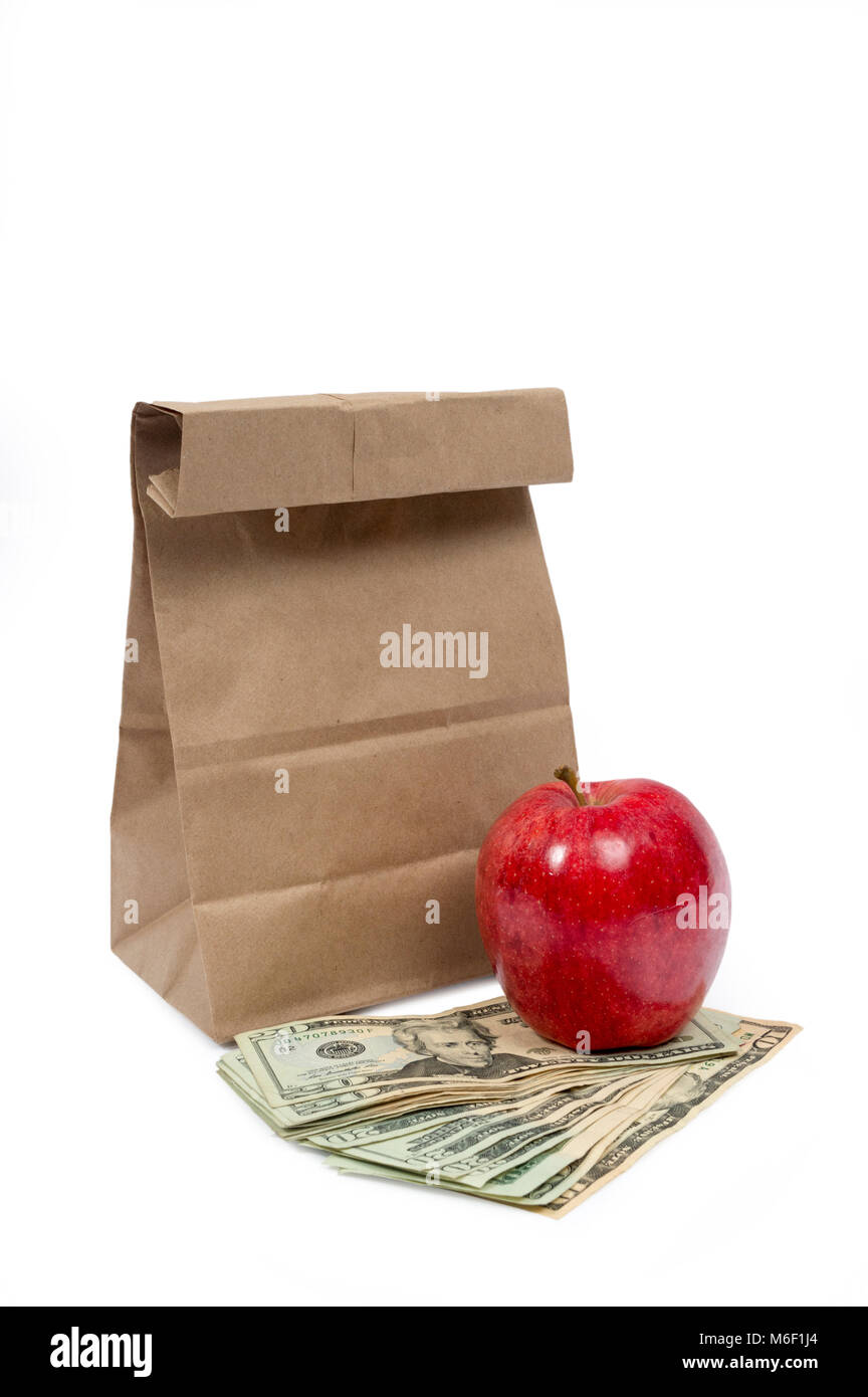 Vertical shot of the front of a brown paper bag with the top folded down with a red shiny apple sitting on fanned out twenty dollar bills and a ten do Stock Photo