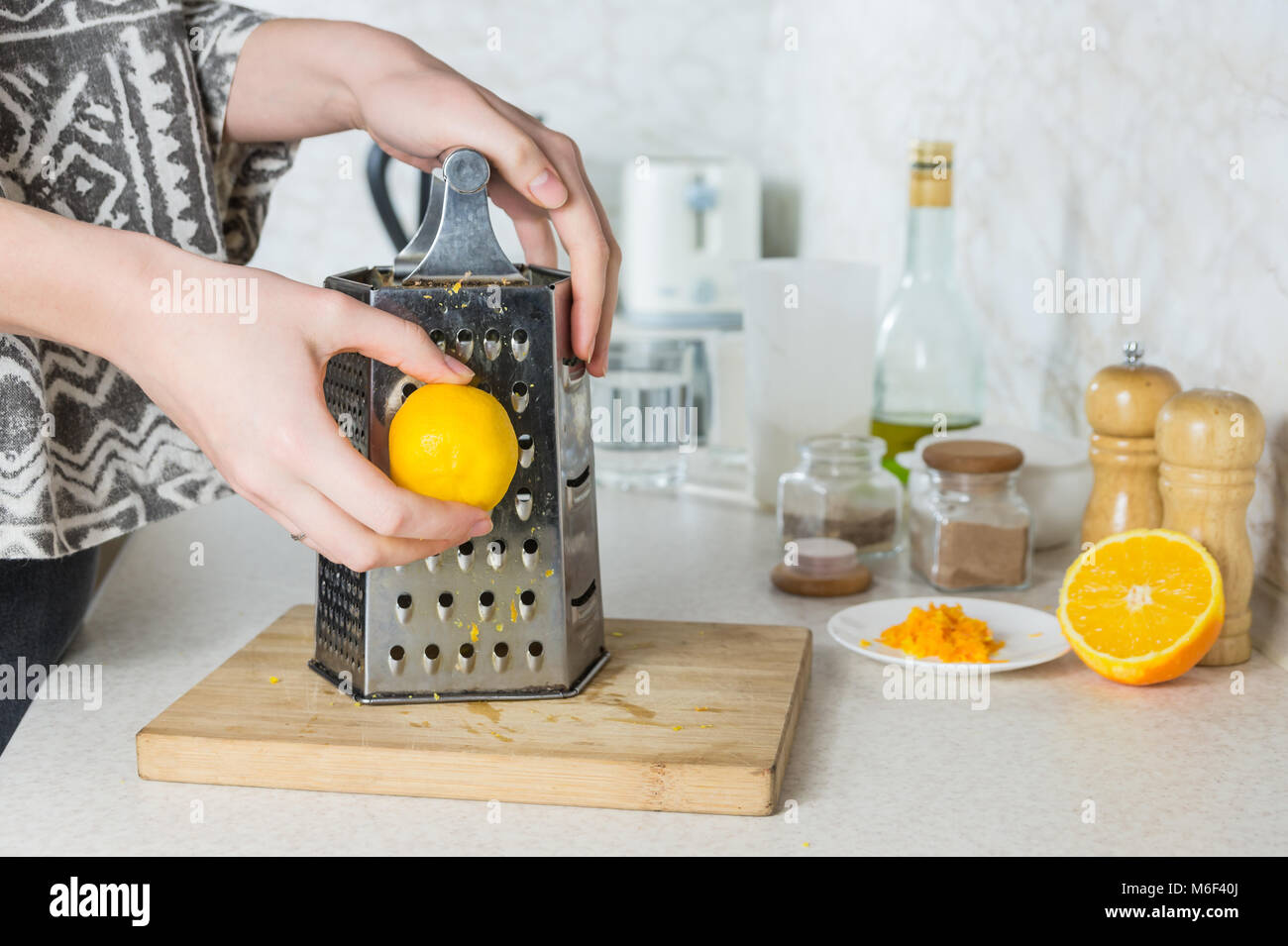 Grating citron zest. Female hands use grater to make lemon peel in kitchen environment Stock