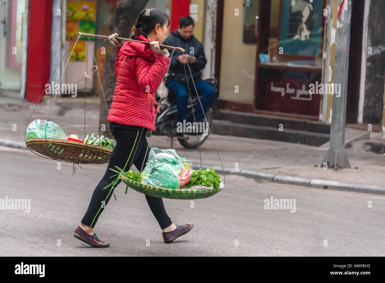 A woman carries vegetables in baskets slung from her bamboo carrying pole in Hanoi, Vietnam Stock Photo
