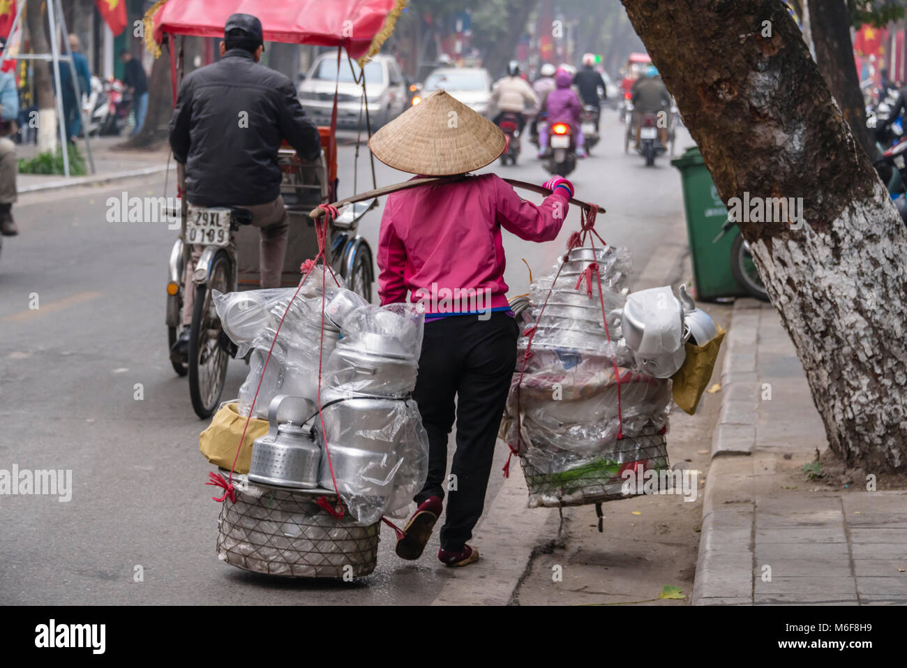 A woman carries aluminium pots and pans to sell in baskets slung from her bamboo carrying pole