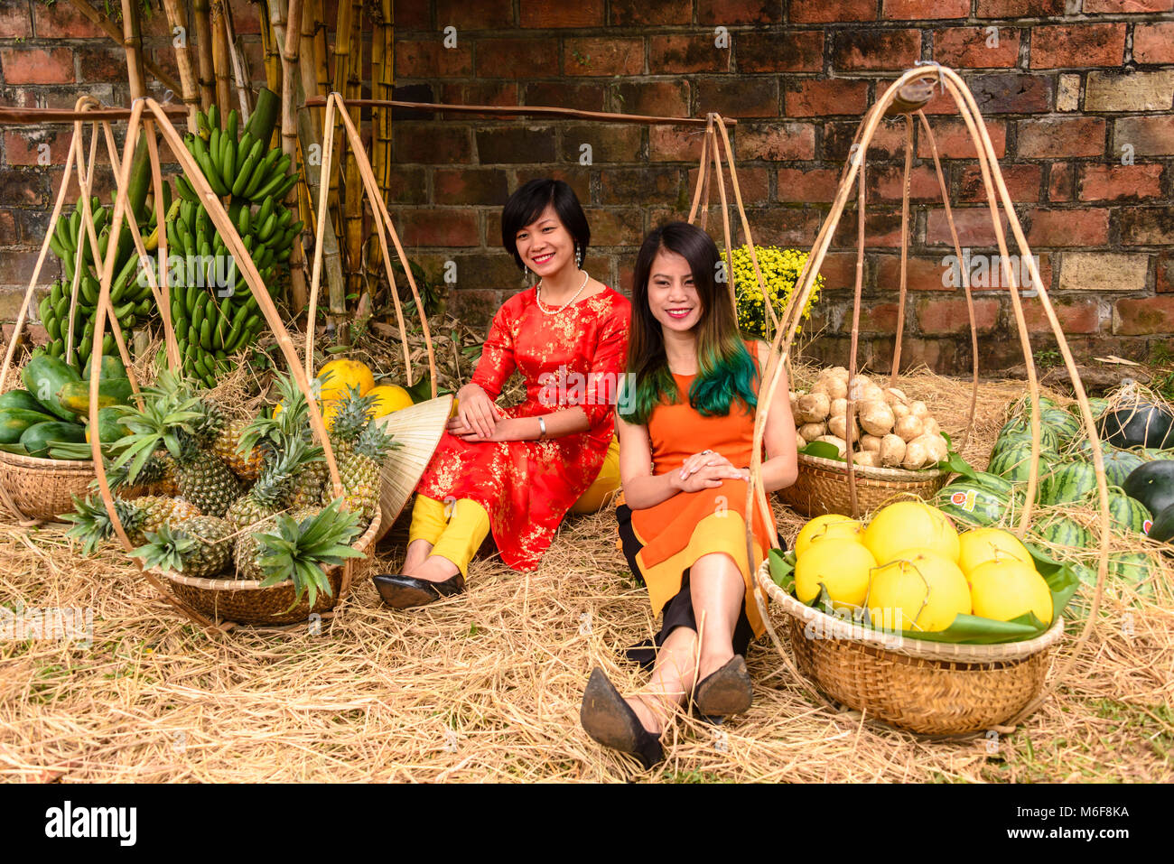 Two women sit among bamboo carrying baskets and poles filled with fruit in Hanoi, Vietnam as they celebrate the Chinese New Year. Stock Photo