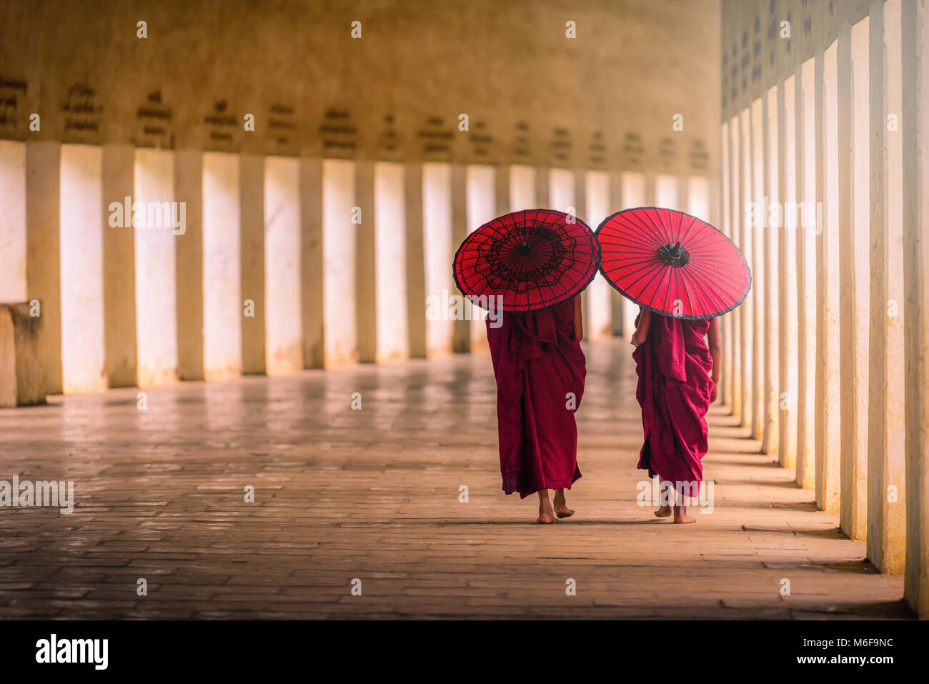 Two buddhist monk novice holding red umbrellas and walking in pagoda, Myanmar. Stock Photo