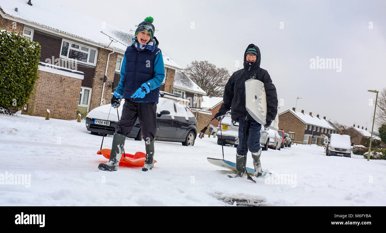 Two boys walk on a snow covered street pulling sledges and body boards to go and play in the March snow and make the most of school closure. Stock Photo