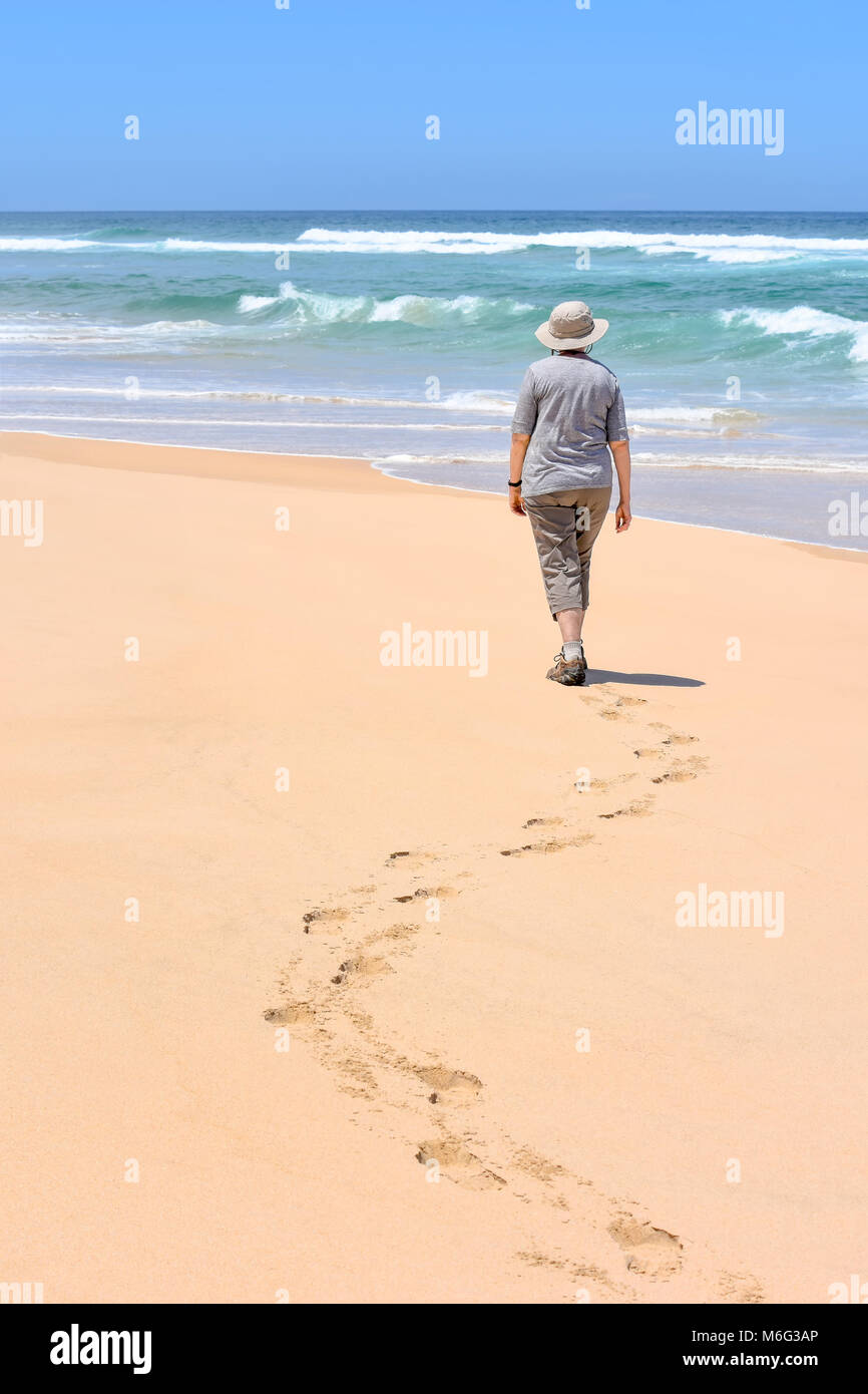 A female on a clean beach at Goukamma near Knysna on the garden route in South Africa walking in isolation with foot steps in the sand into the Indian Stock Photo