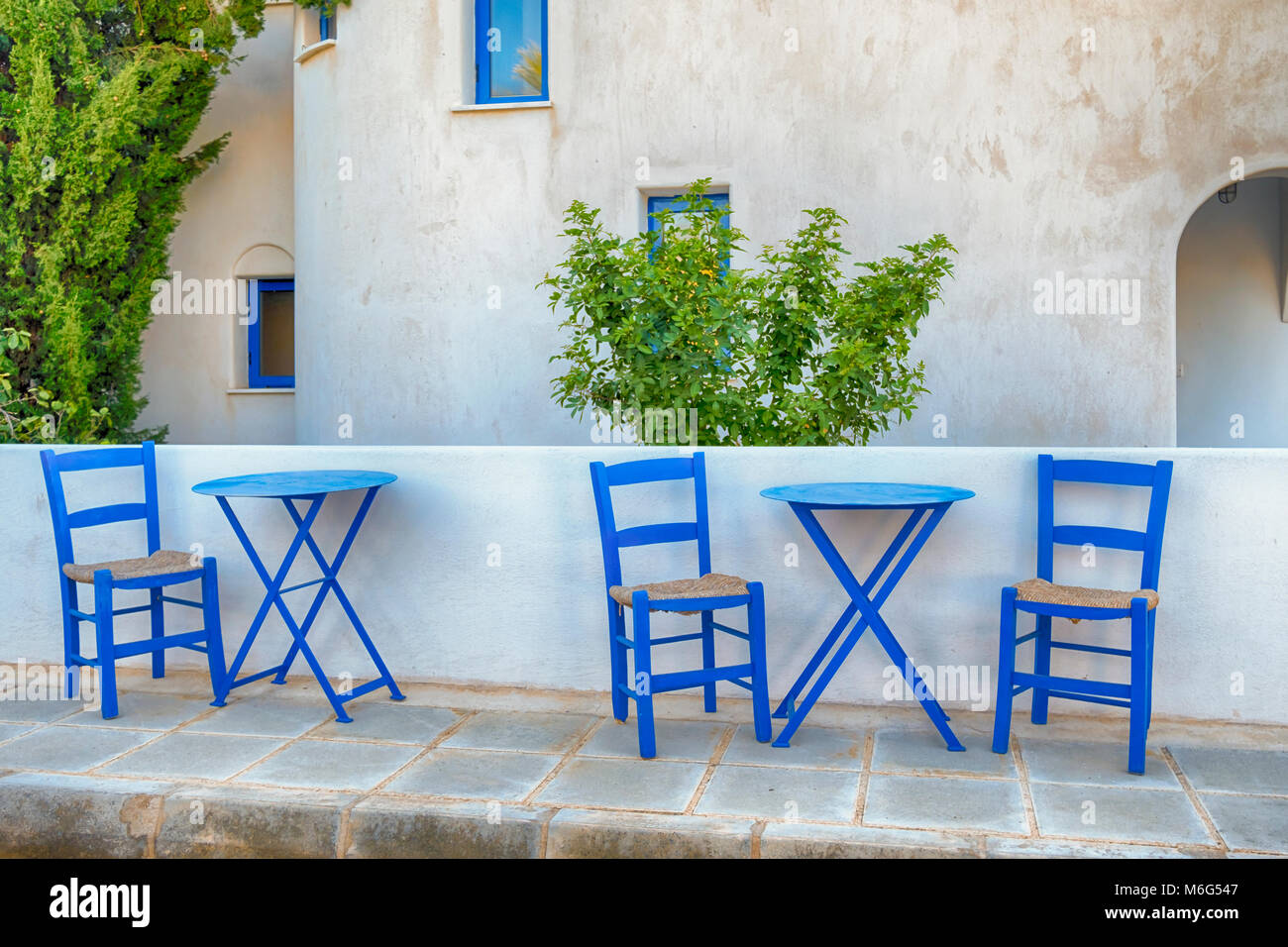 old greek blue chairs with wicker seating on a sun-drenched terrace at a vacation destination Stock Photo