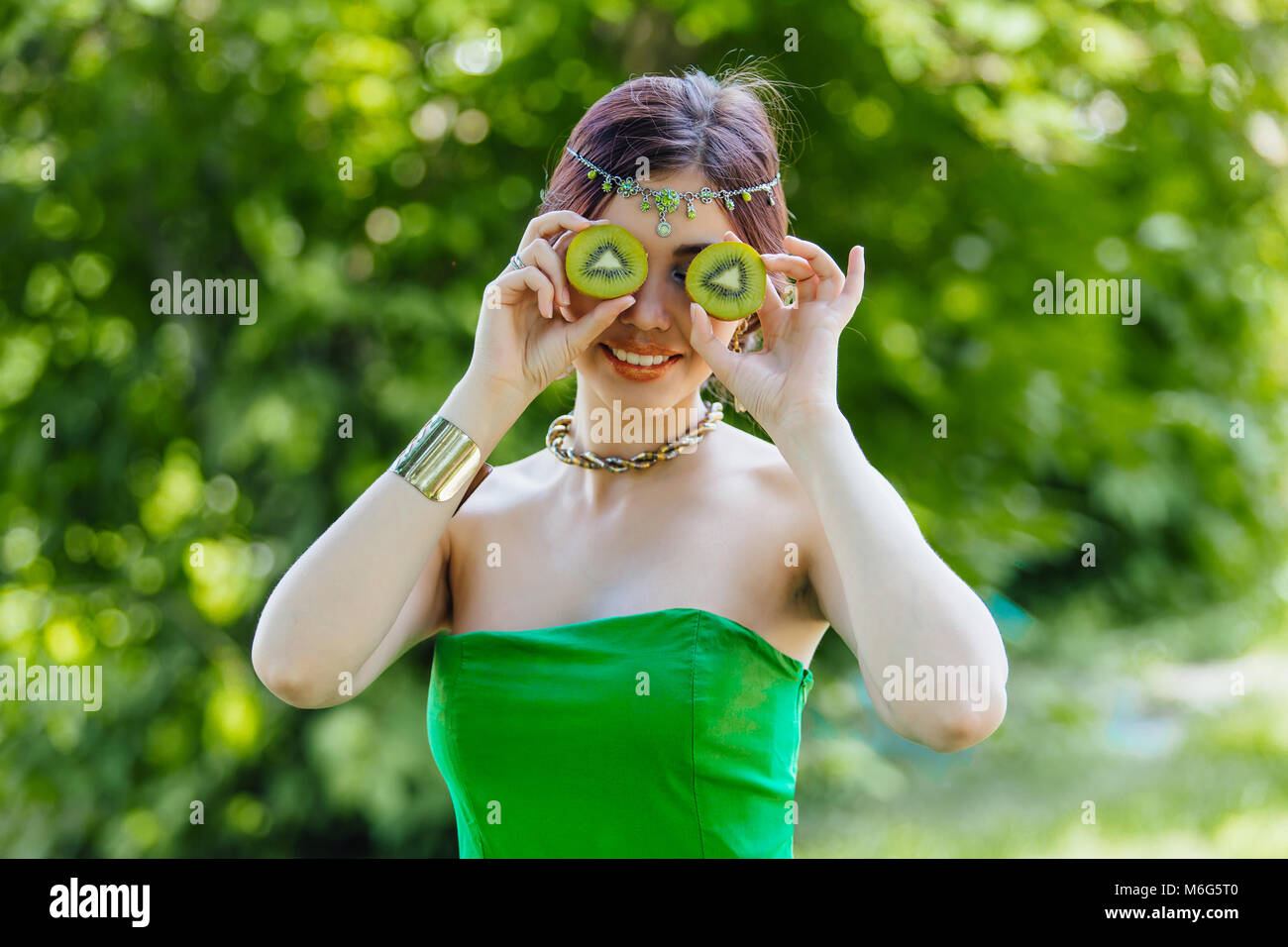 Portrait of a beautiful young asian woman holding two halves of kiwi ...