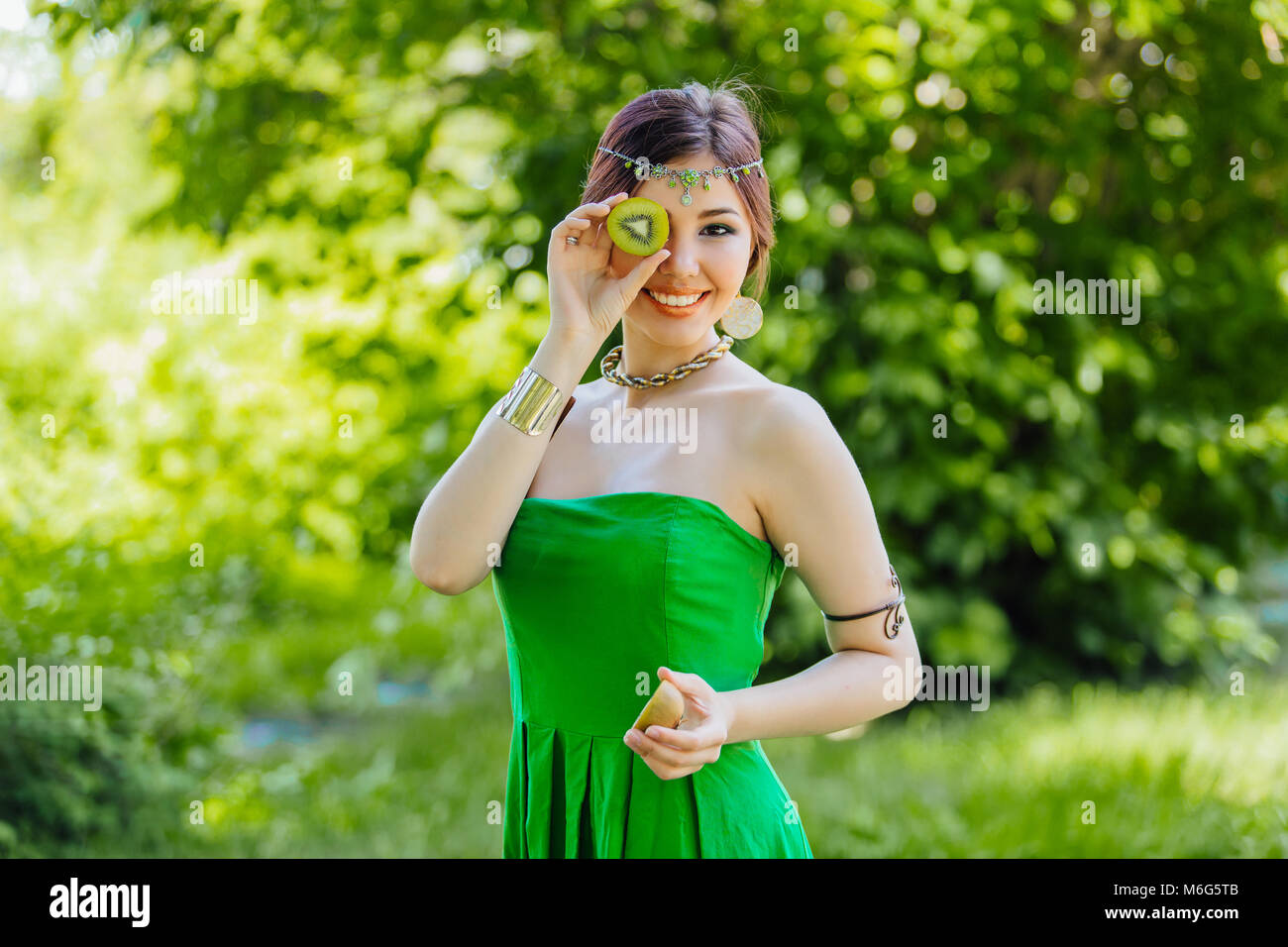 Portrait of a beautiful young asian woman holding two halves of kiwi ...