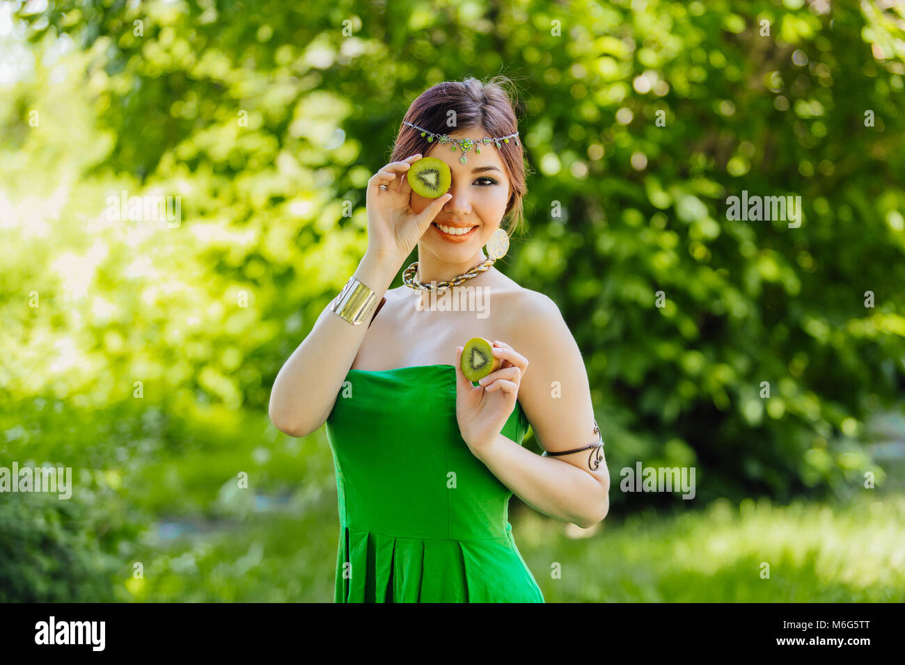 Portrait of a beautiful young asian woman holding two halves of kiwi ...