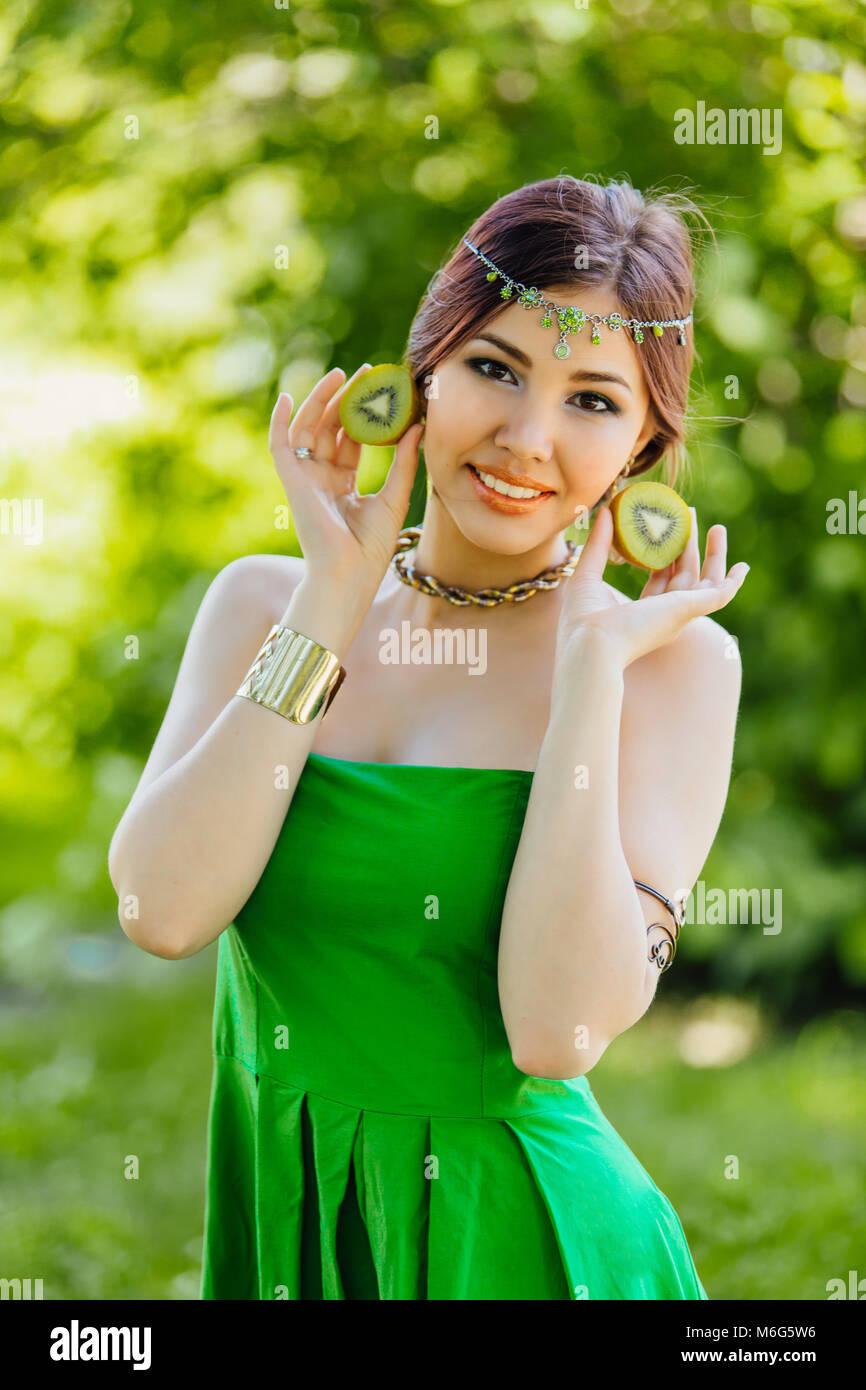 Portrait of a beautiful young asian woman holding two halves of kiwi ...