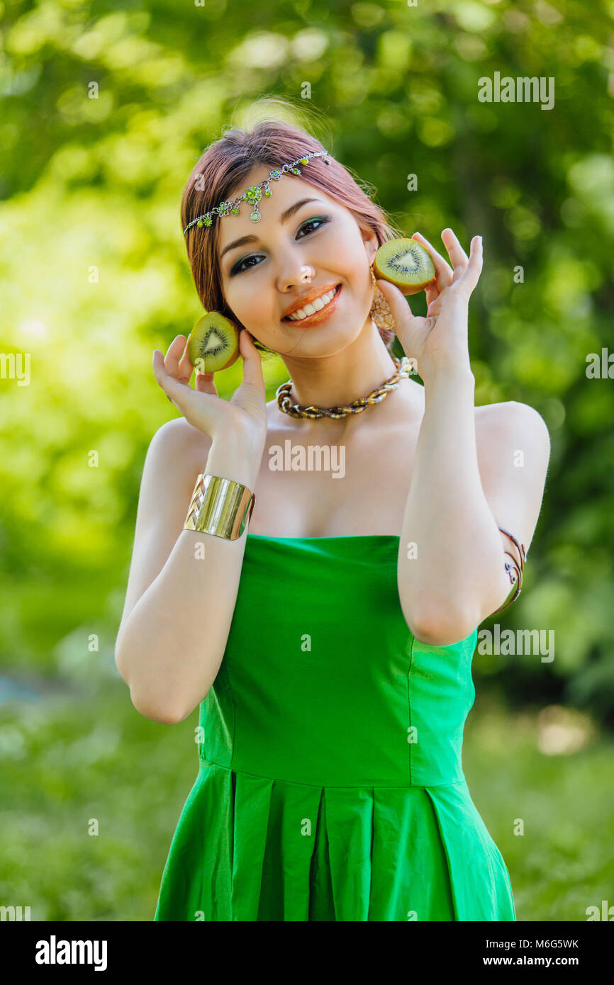 Portrait of a beautiful young asian woman holding two halves of kiwi ...