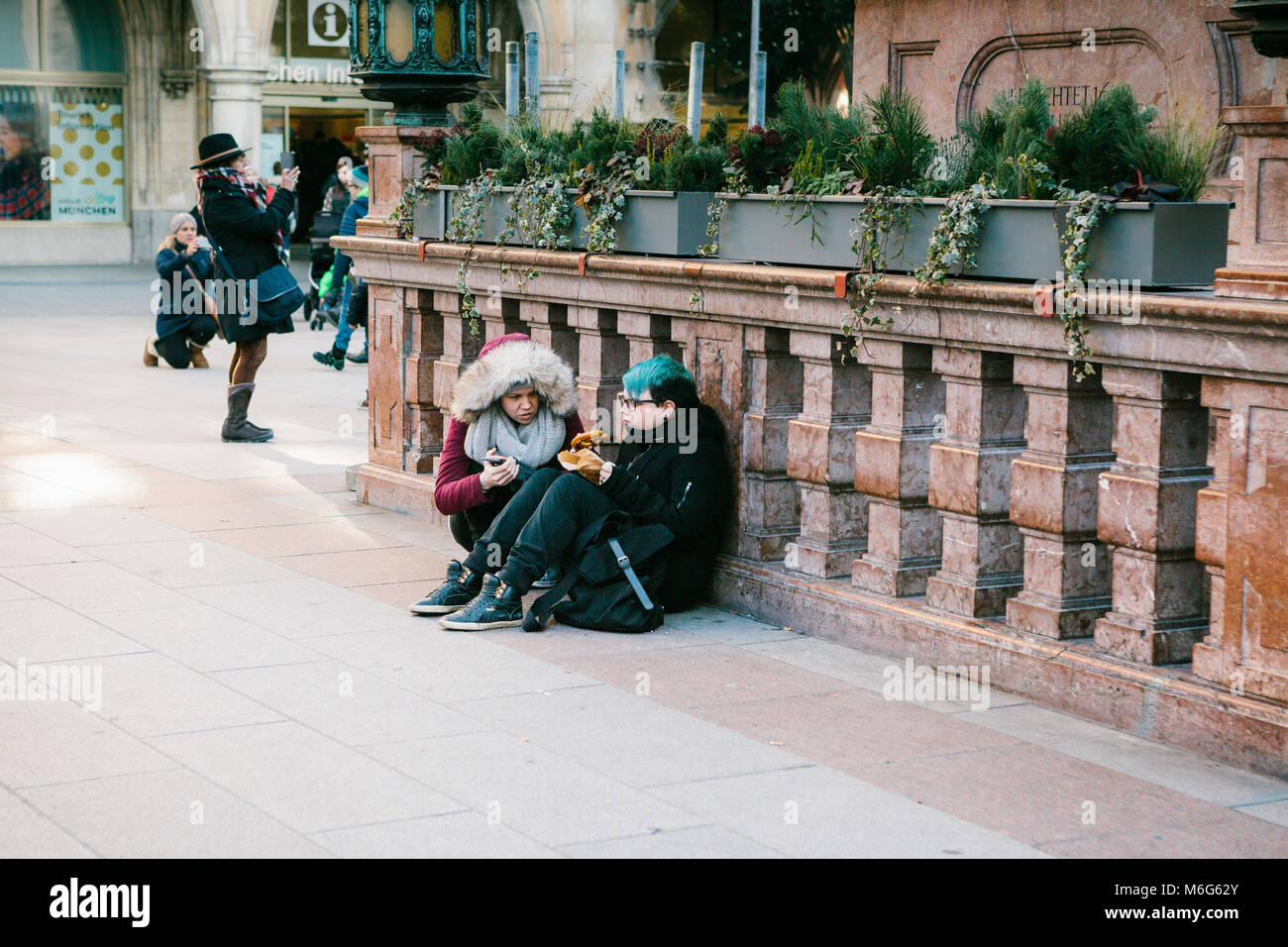Munich, Germany, December 29, 2016: Two punk girls sit and eat in the central square in Munich. Subculture. Everyday routine life in Europe. Homeless, rebels. Stock Photo