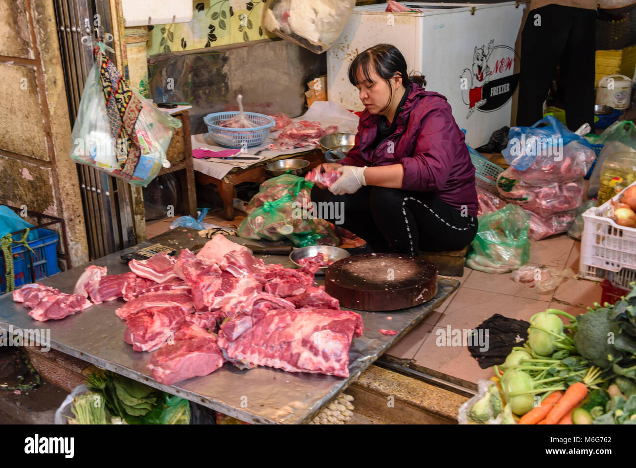 A woman cuts up meat on the floor of her shop and footpath in Hanoi, Vietnam Stock Photo