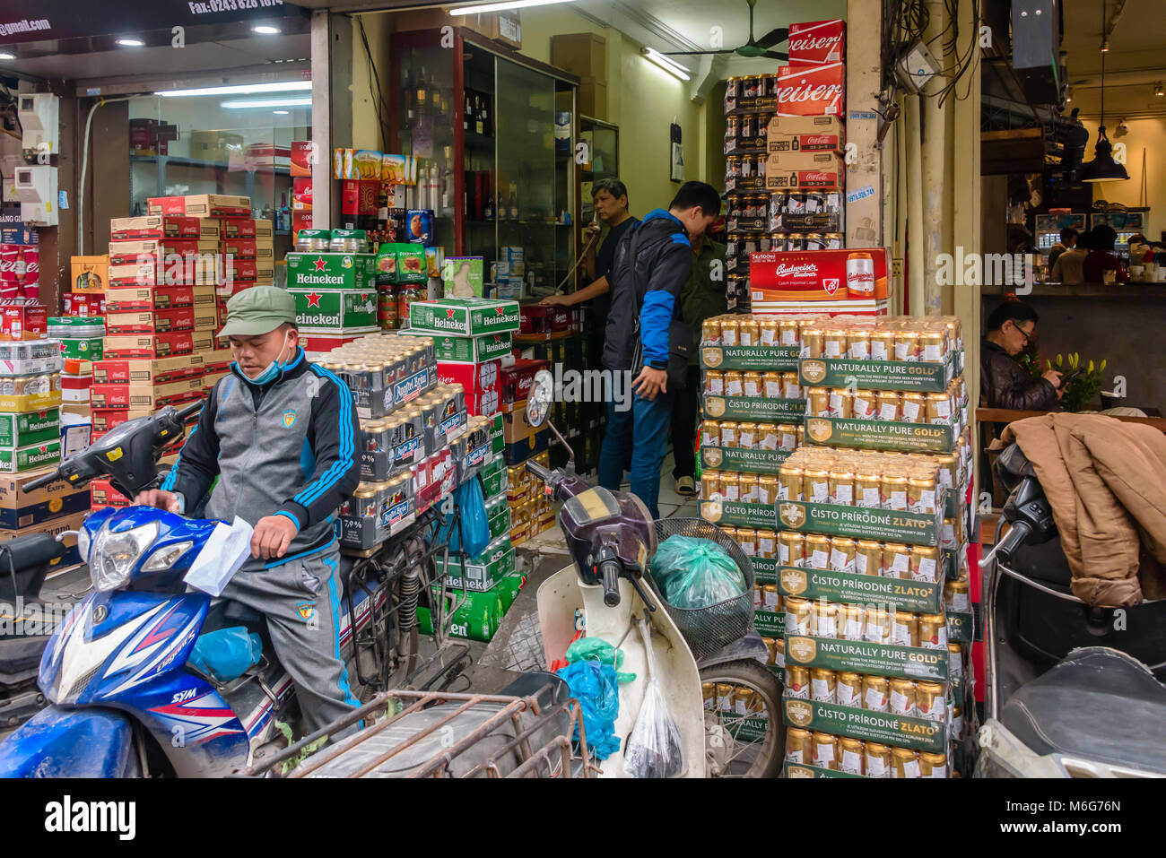 A man leaves a shop selling beer with six cases of beer balanced on the back of his scooter in Hanoi, Vietnam Stock Photo