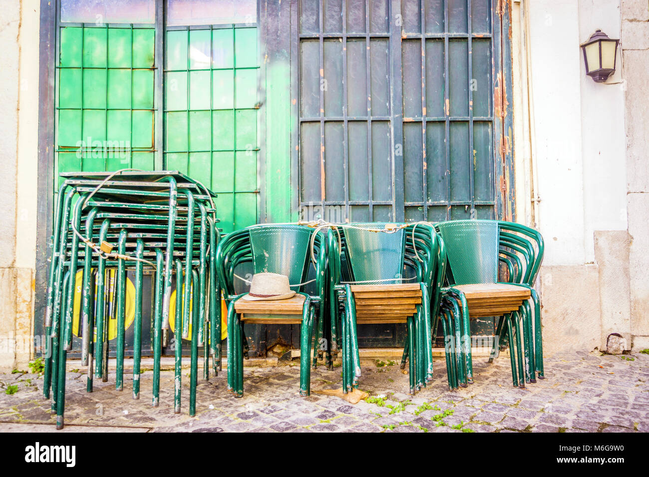 Stacked and locked green tables and chairs on Lisbon old street, Portugal Stock Photo