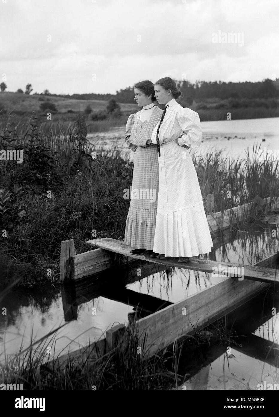 Sisters strike a pose on boards positioned over a waterway, ca. 1900. Stock Photo