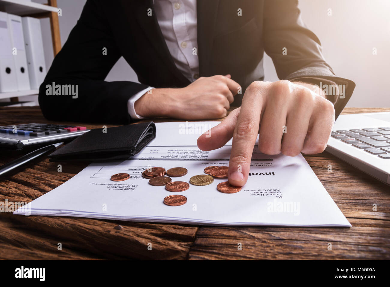 Businessperson's Hand Counting Coins With Wallet And Bill On Wooden Desk Stock Photo