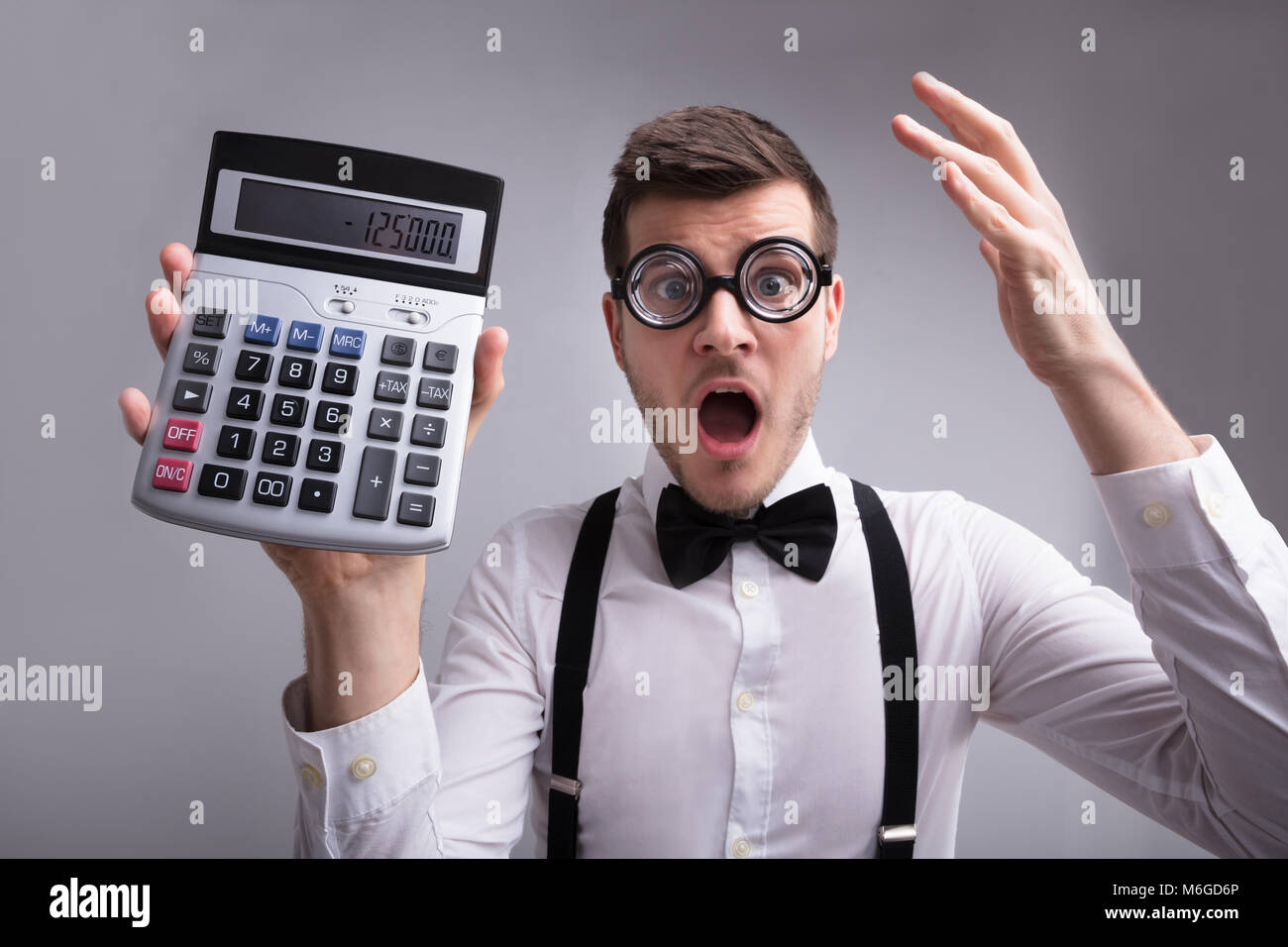 Shocked Young Man Holding Calculator On Grey Background Stock Photo
