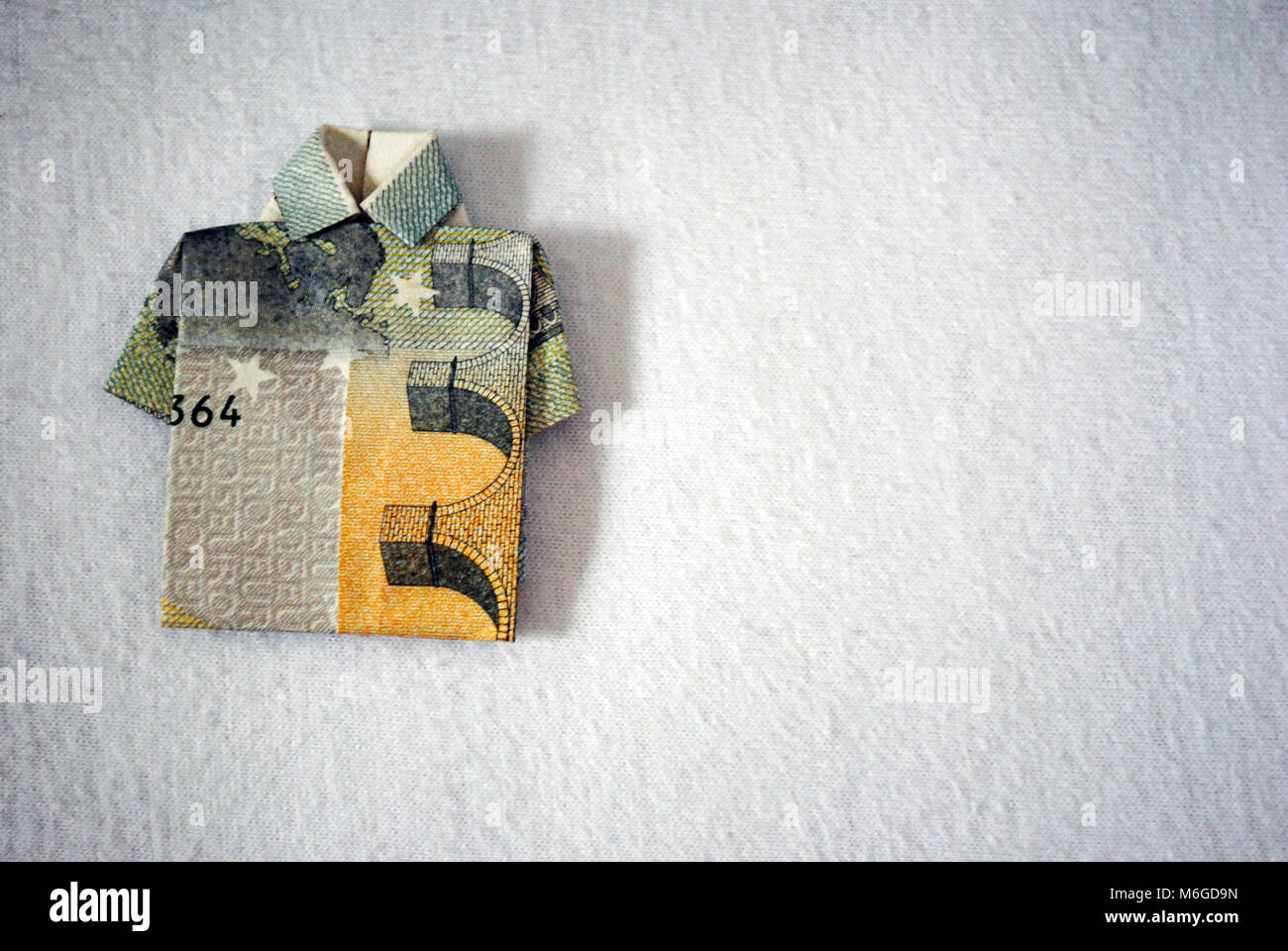 A five euro note folded into a T-shirt shape on white background. Stock Photo