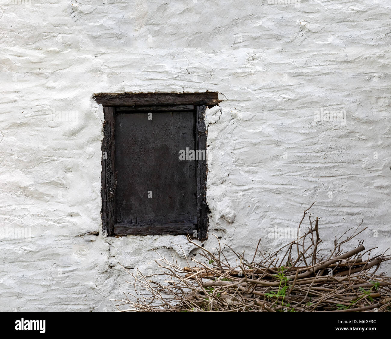 Black old  wooden weathered window on a whitewashed wall . Pile of twigs in the front. Stock Photo
