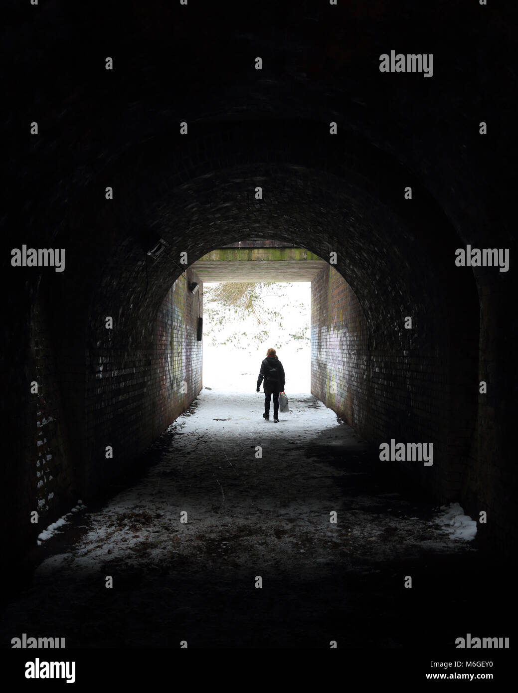 Woman on her own walking through a dark tunnel under a railway line. Stock Photo