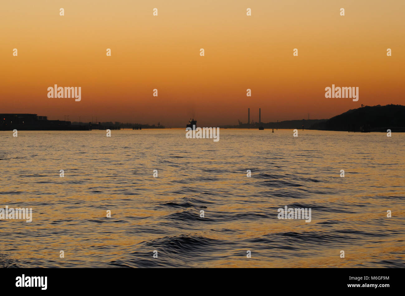 View from a Elbe ferry at sunset. Chimneys of power plant Wedel in the background as silhouette. Stock Photo
