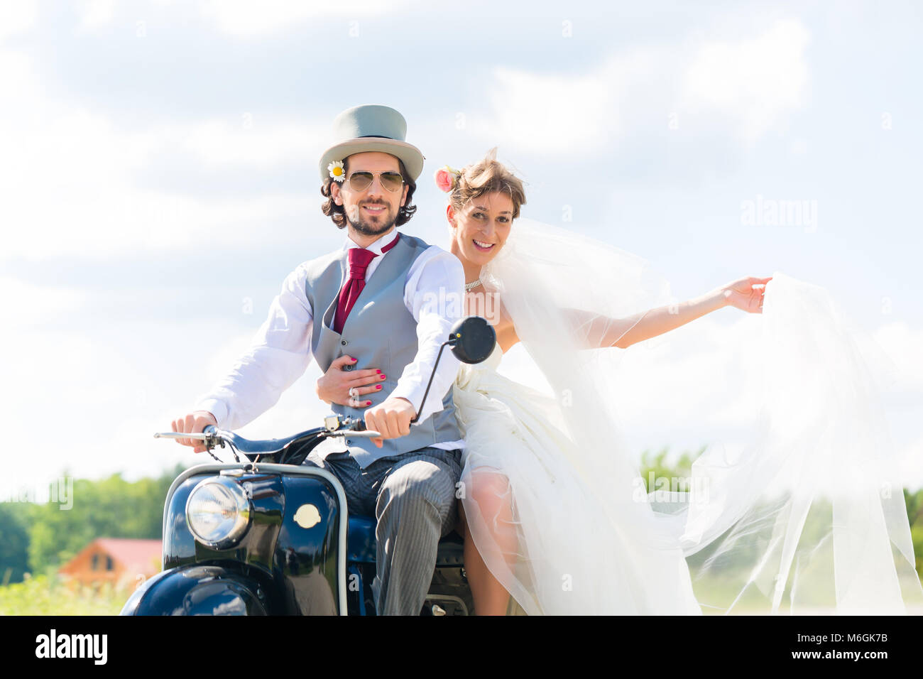 Bridal pair driving motor scooter wearing gown and suit Stock Photo