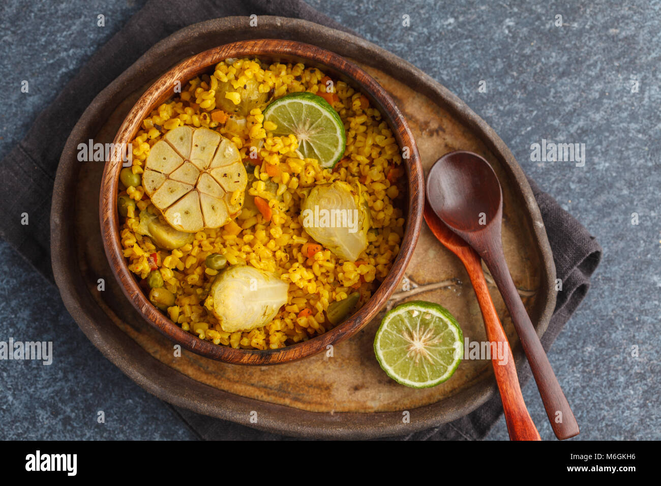 Curry bulgur with vegetables in a wooden bowl. Dark background, vegan meal concept. Stock Photo