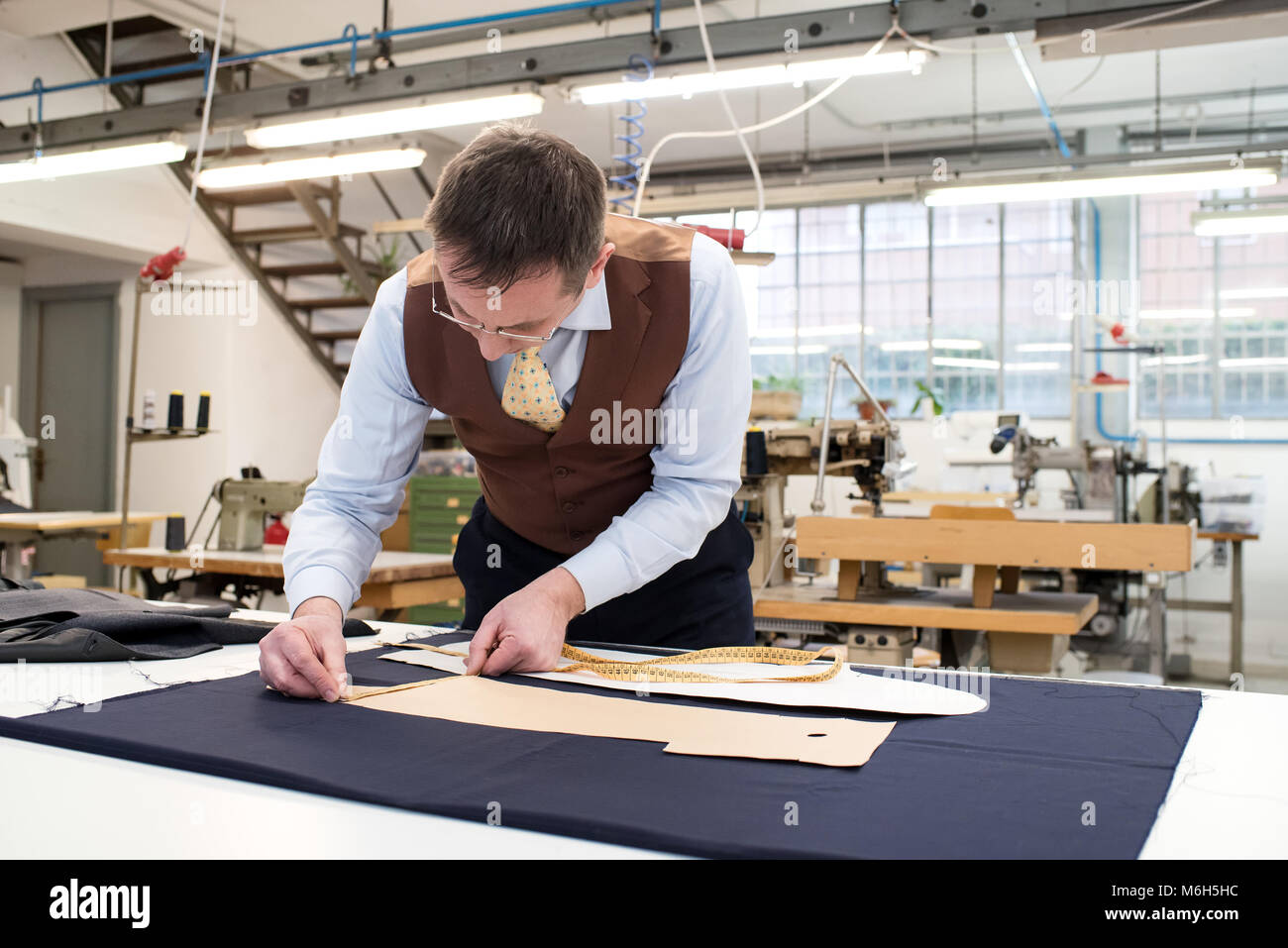 Tailor laying out paper patterns on a bolt of blue fabric laid out on a work table in his workshop measuring the template before cutting the textile Stock Photo