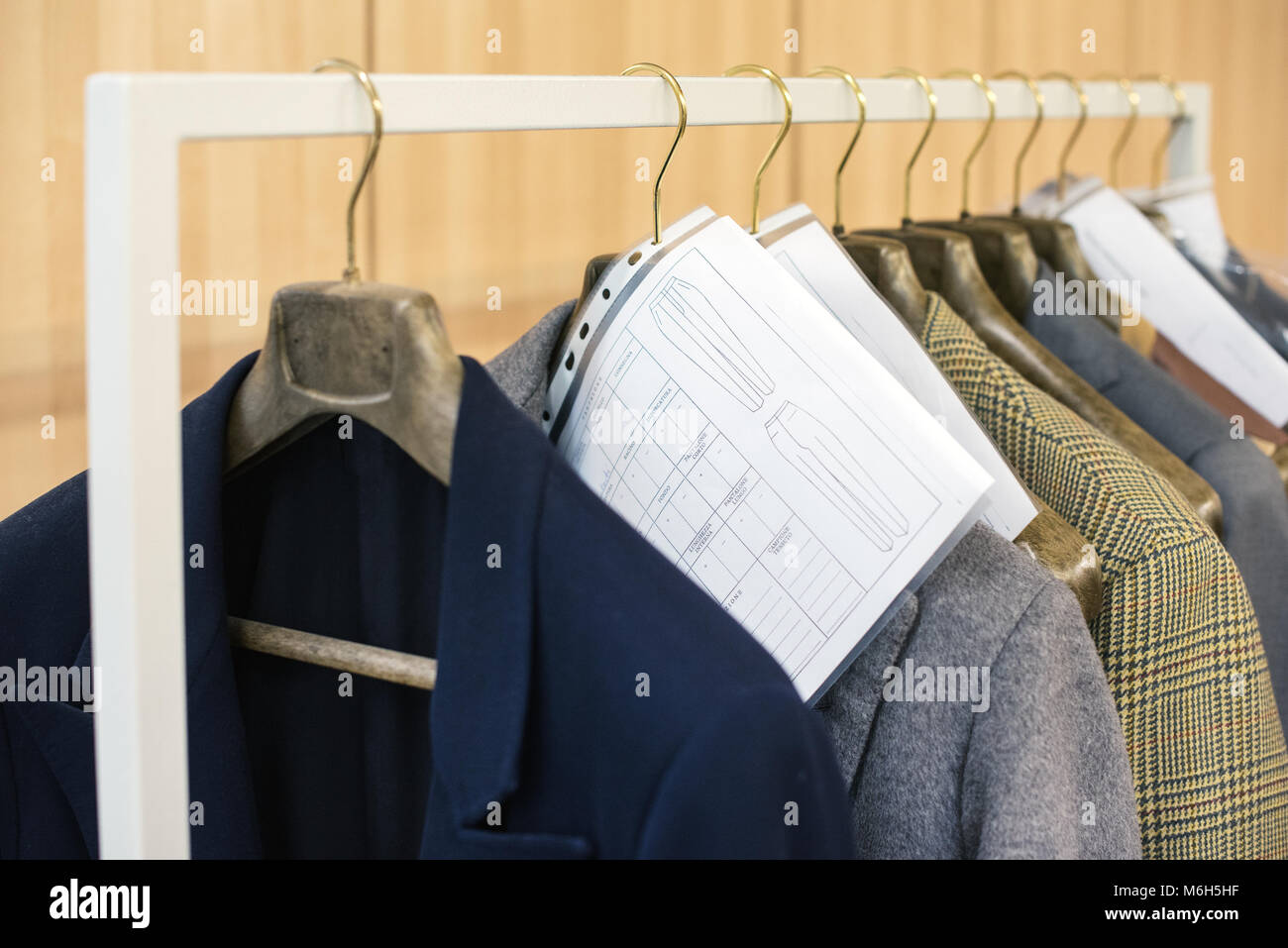 Bespoke tailored jackets hanging on hangers on a rail with their order information and measurements Stock Photo