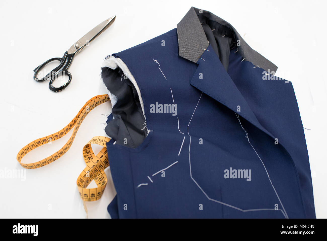 New blue jacket in the process of manufacture showing hand stitching of the pattern lying on a work table in a tailors workshop with scissors and a ta Stock Photo