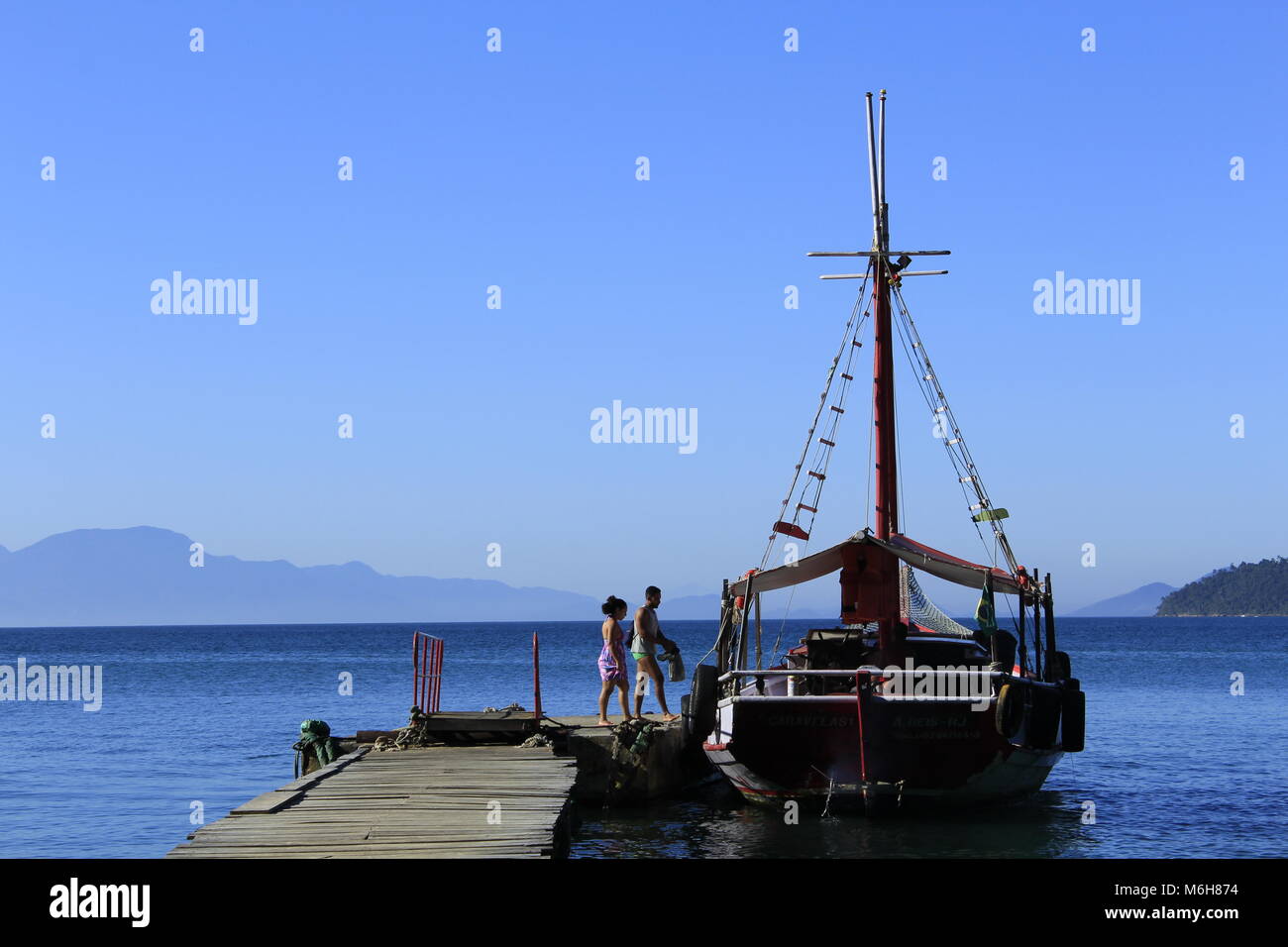 Couple boarding a sailboat docked at a pier in Ilha Grande, Brazil Stock Photo