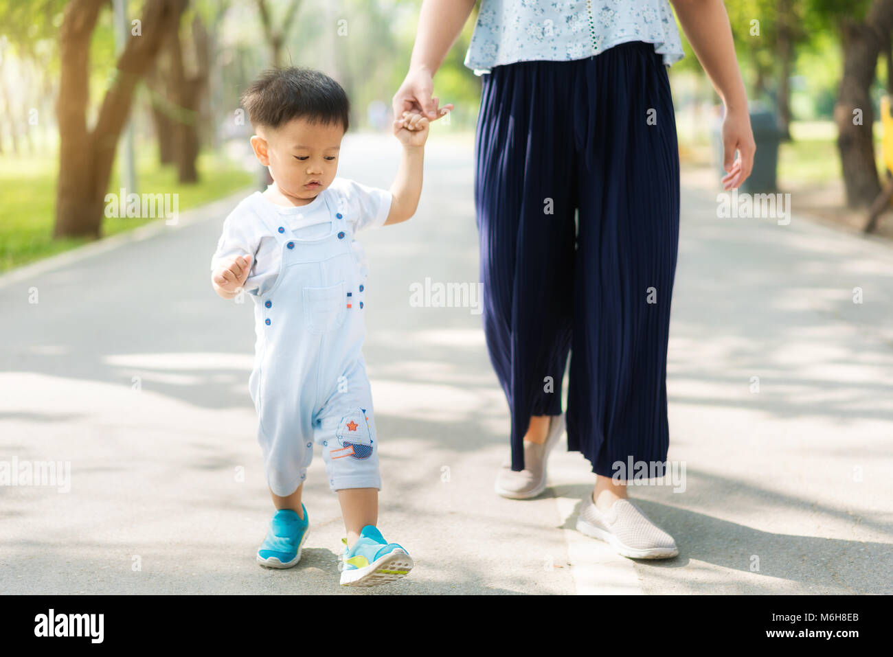 Asian mother walks with her child holding his hand in the spring park. Responsible parenting concept Stock Photo