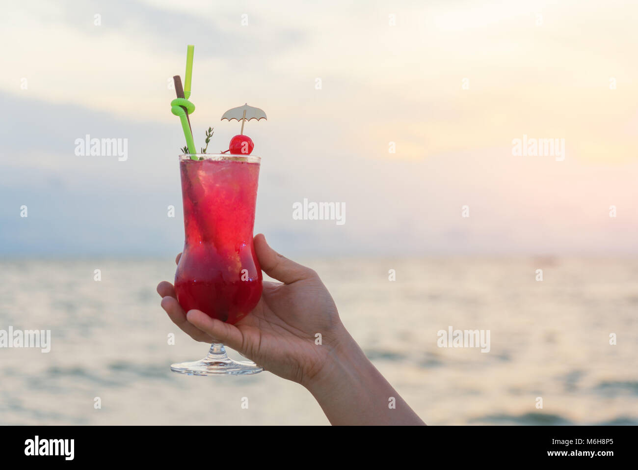 Hand holding red cocktail drink in twilight sea & sky background. Summer, Vacation, Travel and Holiday concept. Stock Photo