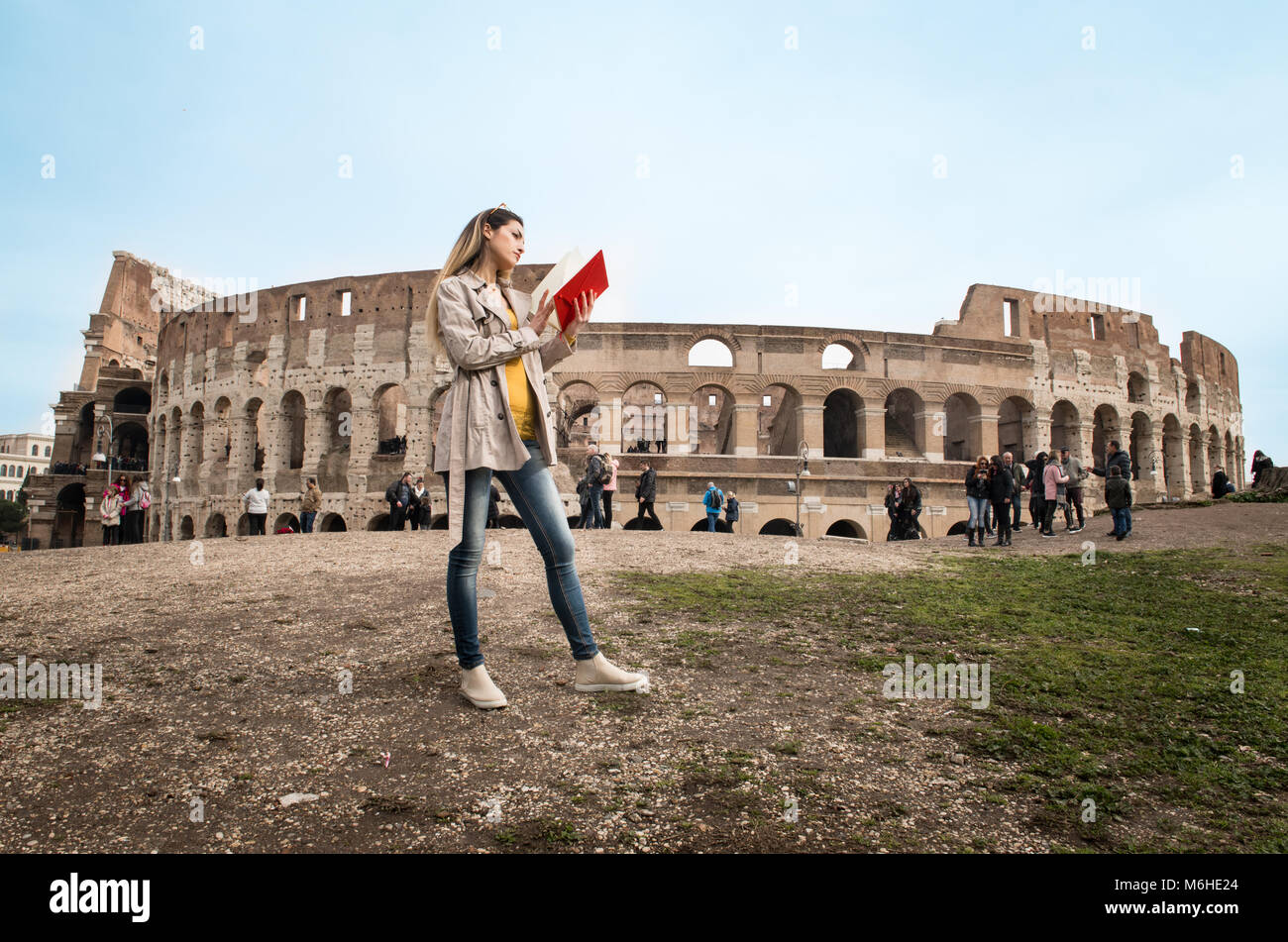 Young pretty tourist woman with travel book reading with colosseum monument in background, Rome Italy Stock Photo