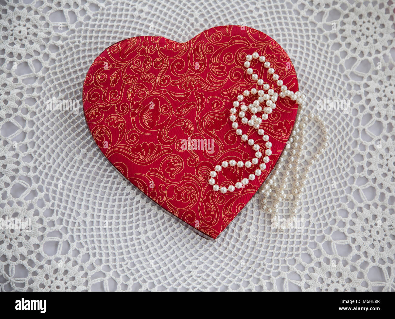 Vintage red fabric Saint Valentine candy box heart against a white doily and pearls, USa, lace Victorian abstract, unconventional Victorian Valentines Stock Photo