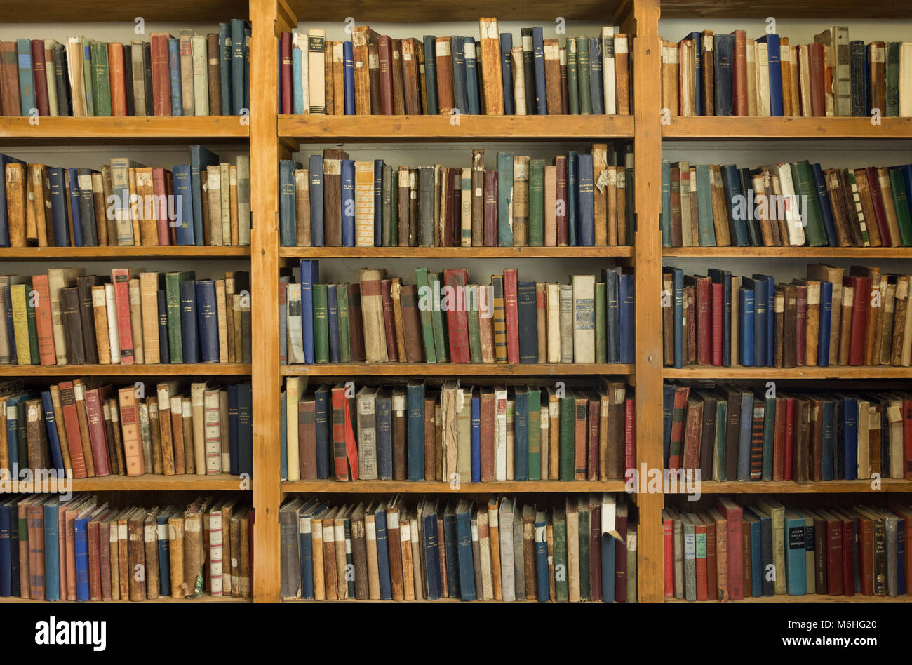 Very old hardcover books with worn bindings on pine shelves in the ...