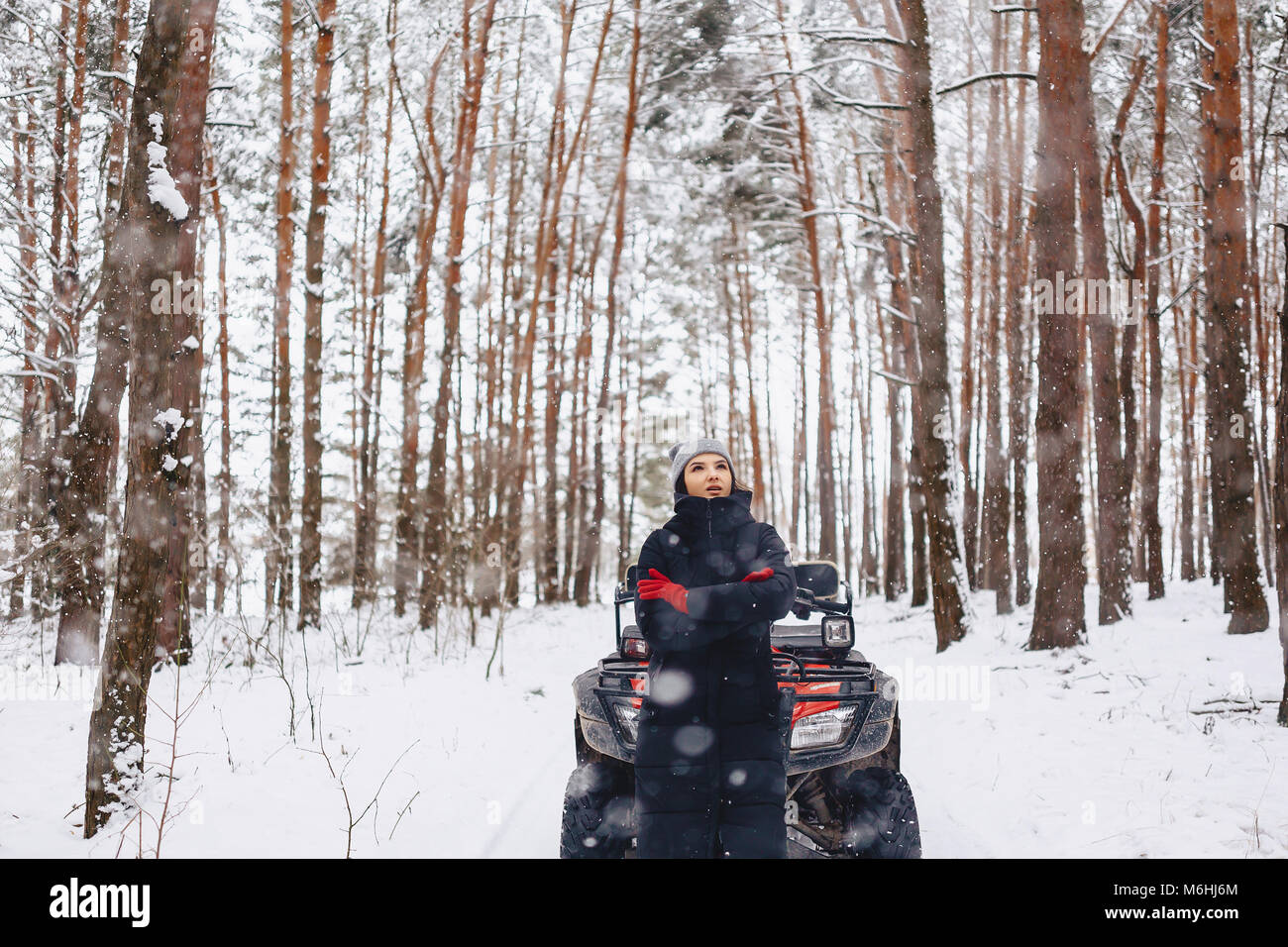 young girl on a motorcycle rides in snow-covered pine forest winters against the background of scenic landscapes Stock Photo