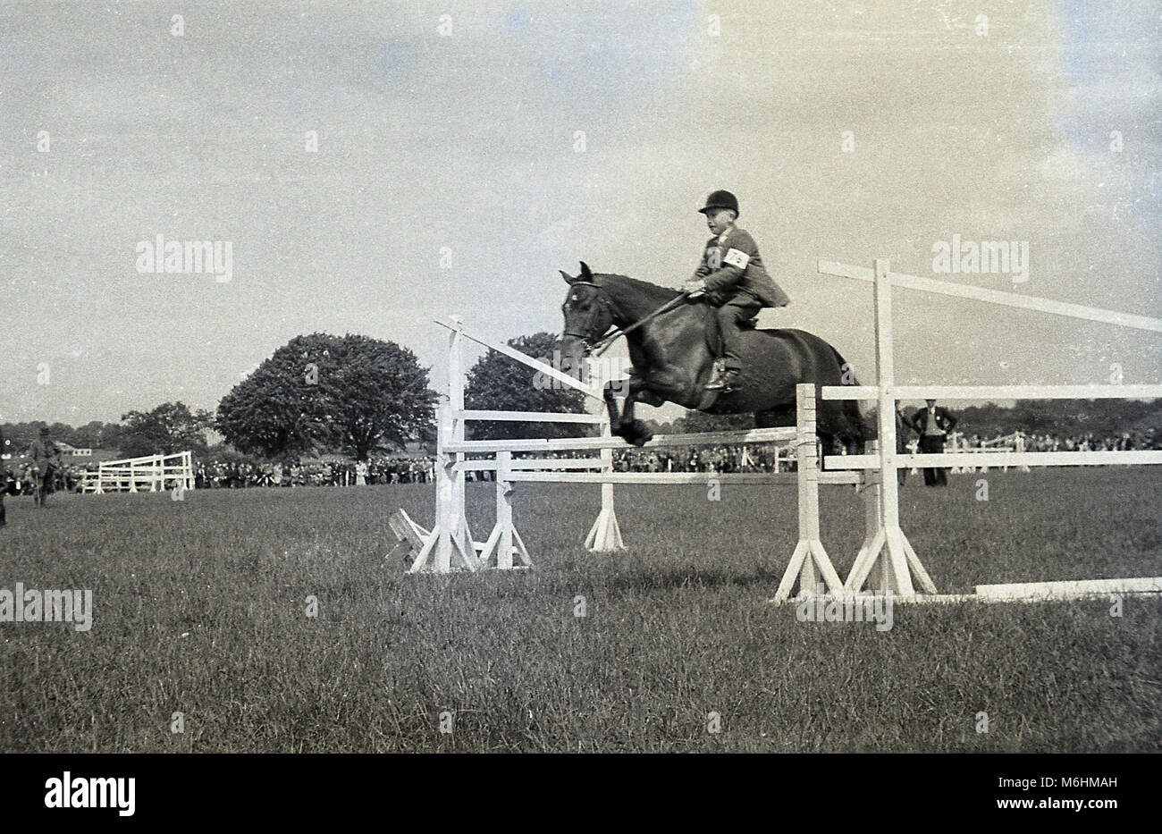 1940s, historical, a young boy riding a horse leaping over an obstacle or fence at an outdoor jumping event, England, UK. Stock Photo